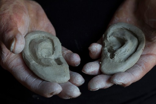 Human head sculpted in clay, hands holding clay ears
