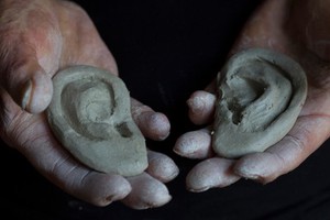 view Human head sculpted in clay, hands holding clay ears