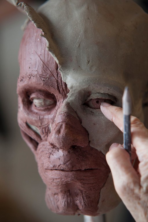 Human head sculpted in clay, completing the eye