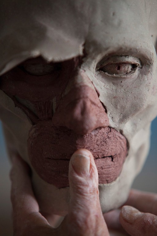 Human head sculpted in clay, completing the mouth