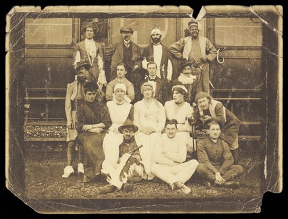 Actors sitting in front of an ambulance train, some in drag. Photograph, 191-.