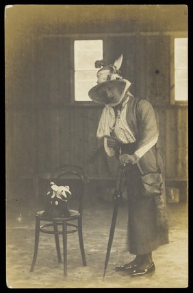 A soldier in drag, dressed in a bonnet and holding an umbrella. Photographic postcard, 191-.