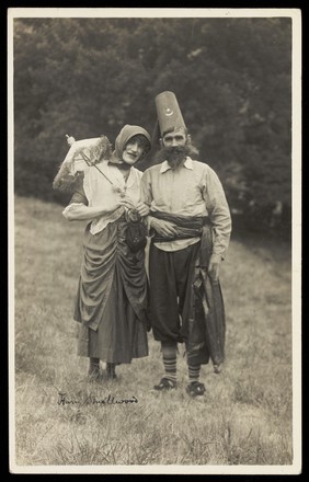 Harry Smallwood and another man stand in a field, one in drag and the other wearing Turkish inspired costume. Photographic postcard, 1925-.