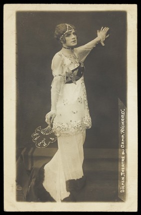 A French prisoner of war acting in an internment camp in Dülmen, performing in drag, wearing a long white dress. Photographic postcard, 191-.