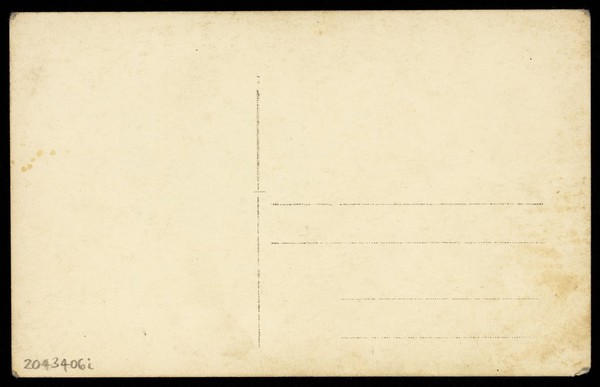 A man in drag wears make-up and is holding flowers, posing for his portrait. Photographic postcard, ca. 1918.