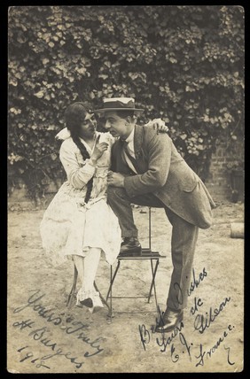Two actors, one in drag, pose on garden furniture. Photographic postcard, 1918.