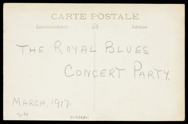 Two soldiers, one in drag called "Miss Billy Timmins", are seated in front of a painted backdrop. Photographic postcard, 1917.