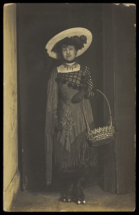 A person wearing a dress, large hat and roller skates, poses holding a basket.