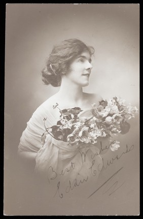 Eddie Edwards, an actor in drag, wearing a white fabric robe, holding a bouquet of flowers. Photographic postcard by L.E. Muller, 191-.