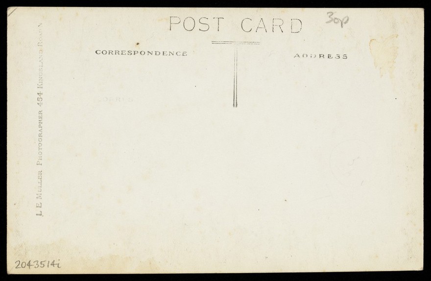 Eddie Edwards, an actor in drag, wearing a white fabric robe, holding a bouquet of flowers. Photographic postcard by L.E. Muller, 191-.