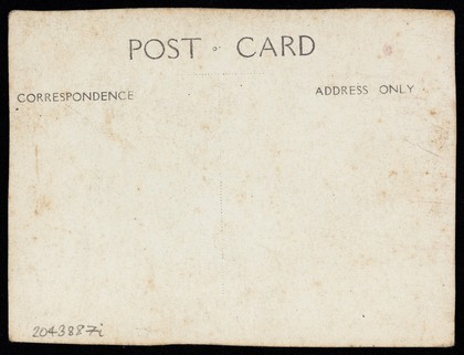 A sailor in drag leans on a high stool, in front of patterned scenery. Photographic postcard, 191-.