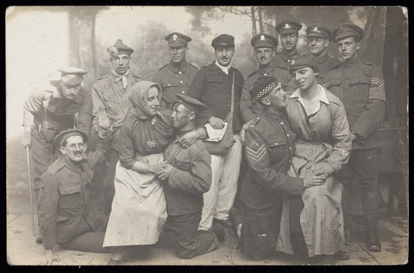 British soldiers, two in drag, pose for a group portrait, in front of a detailed backdrop. Photographic postcard, 191-.