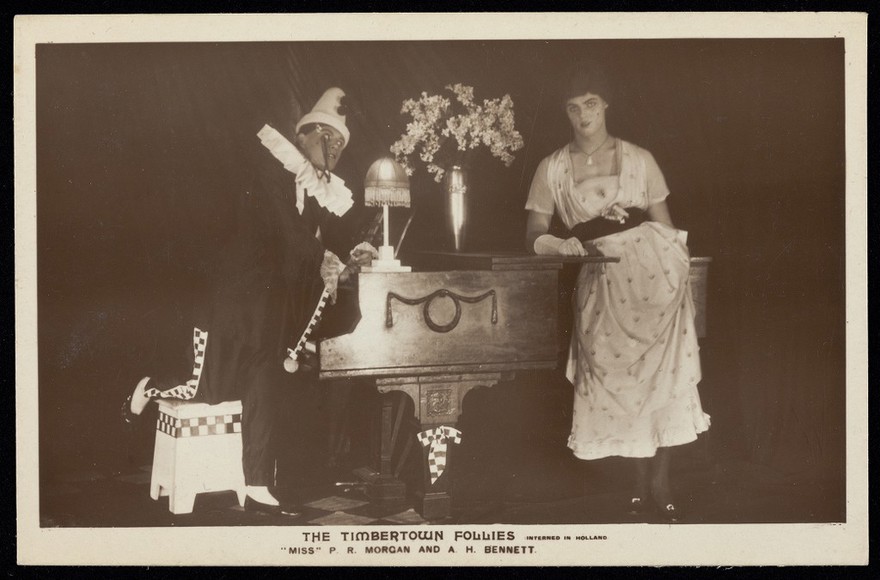 Two British prisoners of war, one in drag, posing for "The Timbertown Follies", at a prisoner of war camp in Groningen. Photographic postcard, 191-.