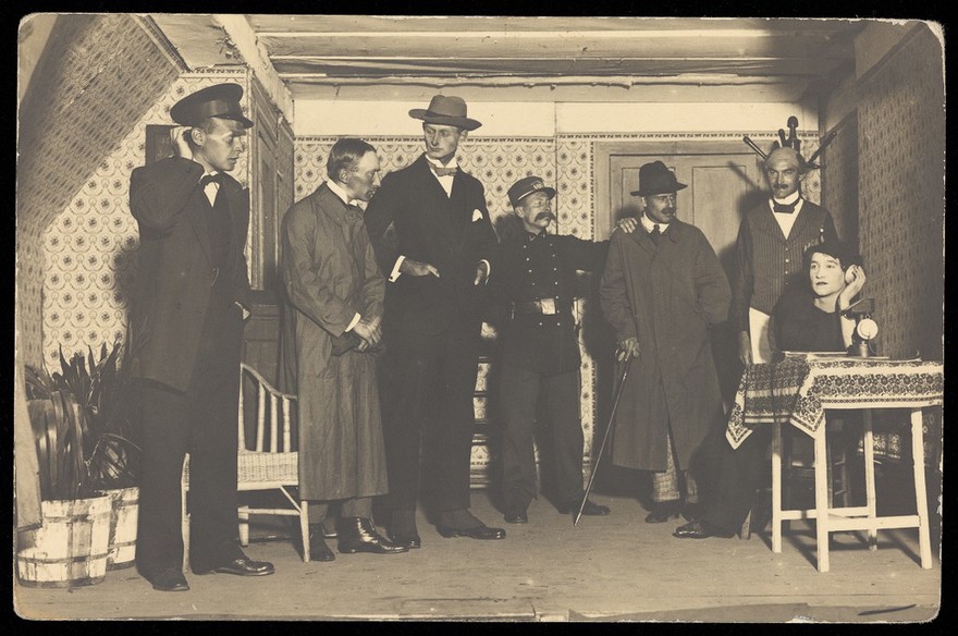 French or Belgian prisoners of war, one in drag, performing a scene from "L'anglais tel qu'on le parle" at Friedberg Camp, Germany. Photographic postcard, 1917.