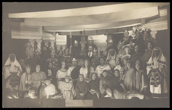 Amateur actors, some in drag, pose on a crowded stage. Photographic postcard, 191-.