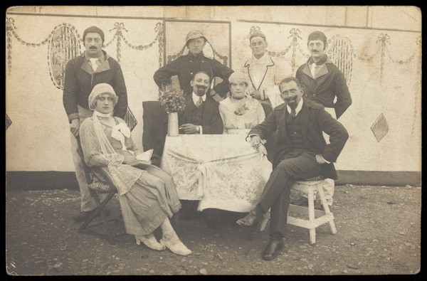 German soldiers, some in drag, pose round a table at a concert party. Photographic postcard, 191-.