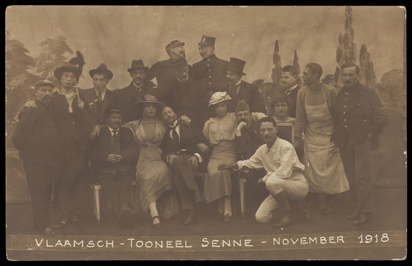 Belgian prisoners of war, some in drag, pose on stage for a group portrait; at Sennelager prisoner of war camp in Germany. Photographic postcard, 1918.