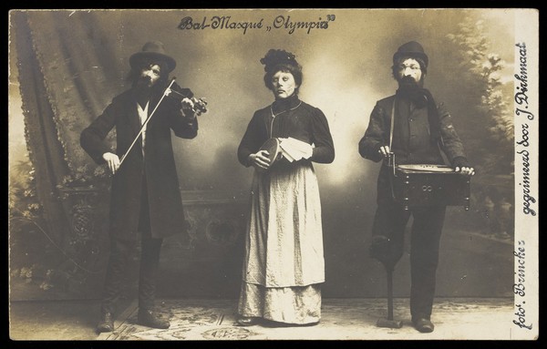 Three musicians, one in drag, in masks for an "Olympia" masked ball.