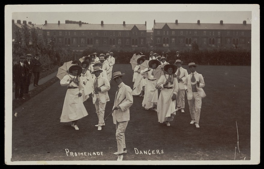 A group of men, some in drag, dancing the Promenade on a lawn.