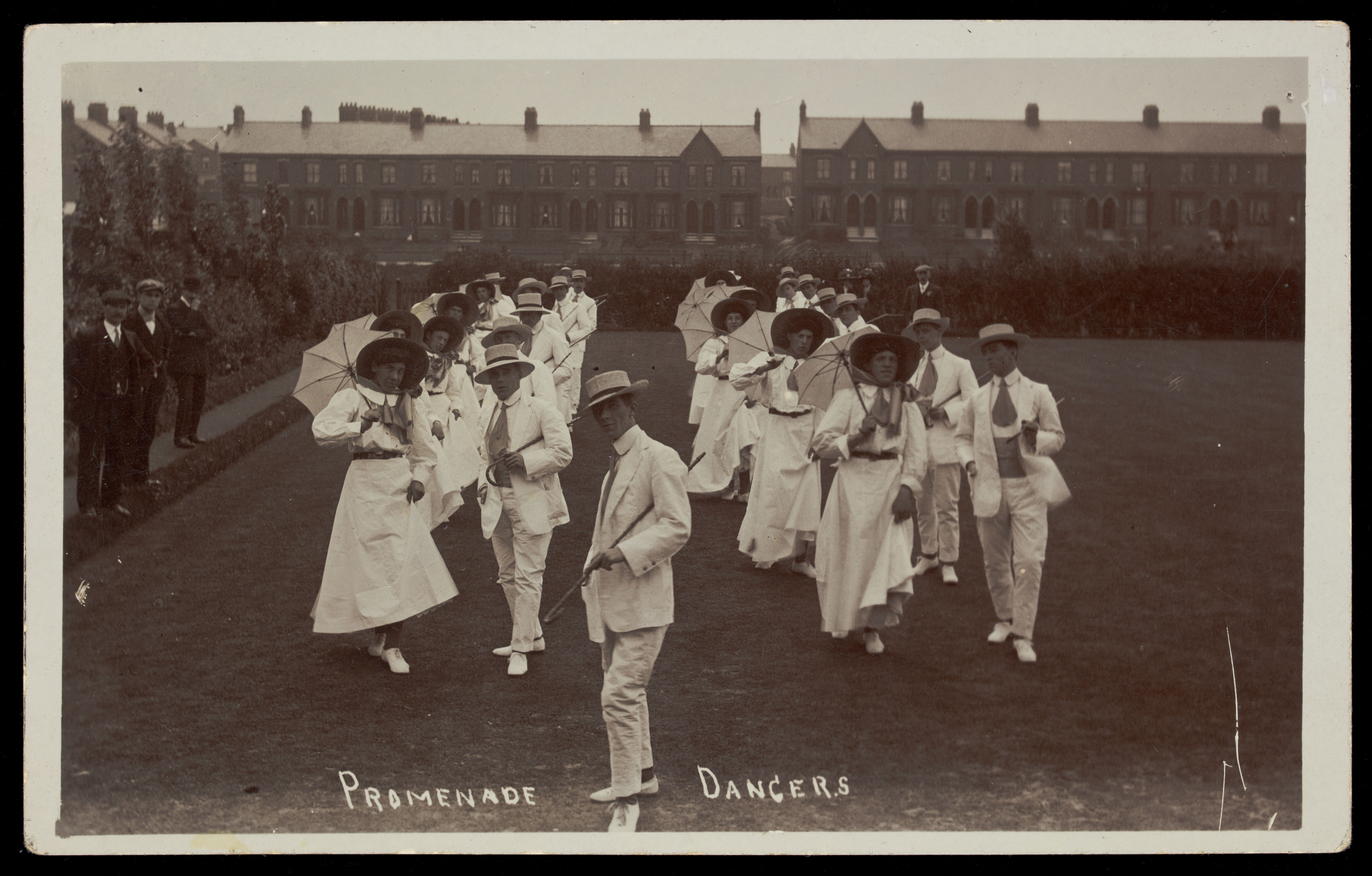 A group of men, some in drag, dancing the Promenade on a lawn.