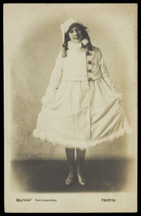 An actor in drag, wearing a white fluffy-trim coat. Photographic postcard by Relph, ca. 1917-1918.