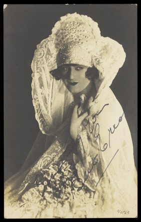 Bert Errol, in character, wearing an elaborate white dress. Process print, 1925.