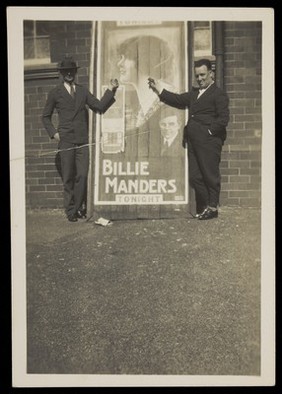 Two members of the Quaintesques pose in front of a poster advertising Billie Manders. Photograph, 192-.