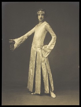 Cecil Beaton, in drag; dressed in a tight-fitting lamé dress. Photograph, ca. 1925.