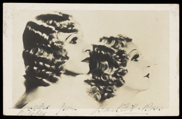 Bartlett and Ross in drag pose in profile, with matching hair and make-up. Photographic postcard, 1937/1938.