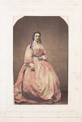 A man in drag poses wearing a large pink dress. Photograph, 189-.