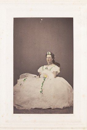 A man in drag is sitting down wearing a large white dress. Photograph, 189-.