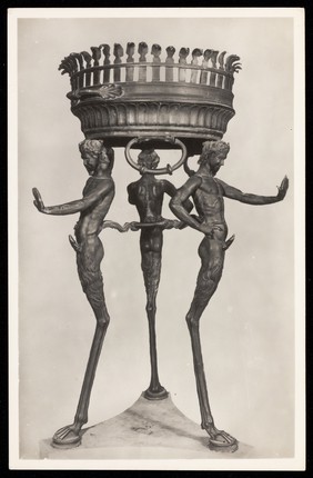 A bronze tripod with three satyrs sculpted for the legs of the tripod. Photographic postcard, 195-.