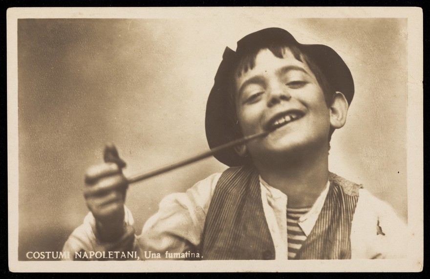 Photograph of a boy in costume smoking a long pipe.