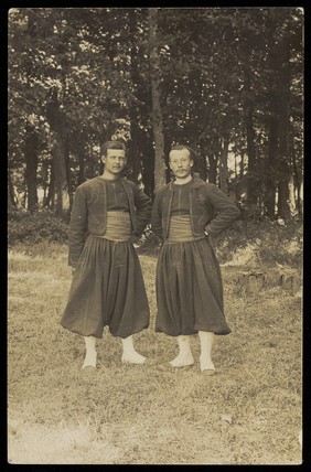 Two men standing side by side in the woods. Photographic postcard, ca. 1910.