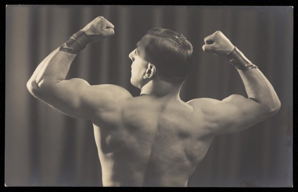 A strongman flexes his biceps, seen from behind. Photographic postcard, 19--.