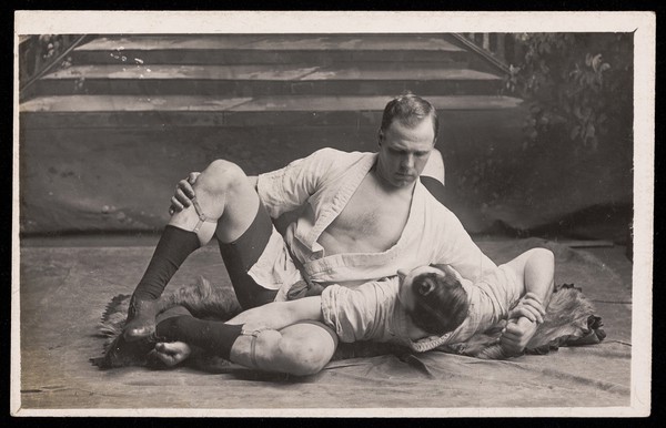 Two male wrestlers fighting on the floor. Photographic postcard, 19--.