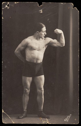 A wrestler flexing his biceps. Photographic postcard, 19--.