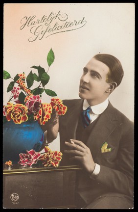 A man admiring a bowl of flowers. Coloured photographic postcard, 192-.