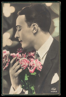 A man holding pink and white flowers. Coloured photographic postcard, 192- (?).