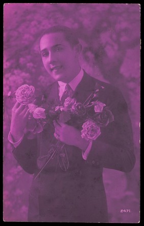 A young man holding roses, engaging the viewer. Colour photographic postcard, 192-.