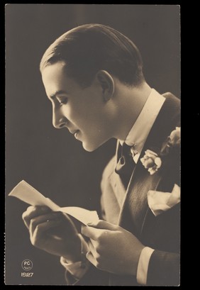 A young man, in profile, reading a note. Photographic postcard, 1927.