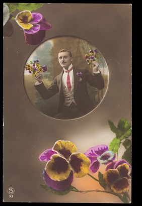 A young man holding flowers inset centrally within a circle, larger flowers are in opposing corners. Coloured photographic postcard, 1919.