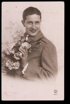 A young man holding flowers. Photographic postcard, 1937.