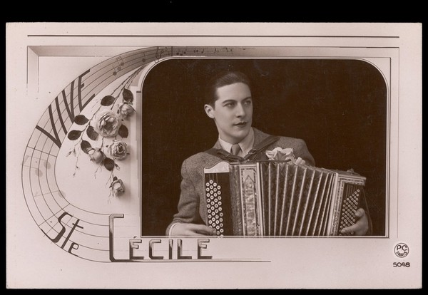 A man holding an accordion with flowers, celebrating Saint Cecilia's Day. Colour photographic postcard, 192-.