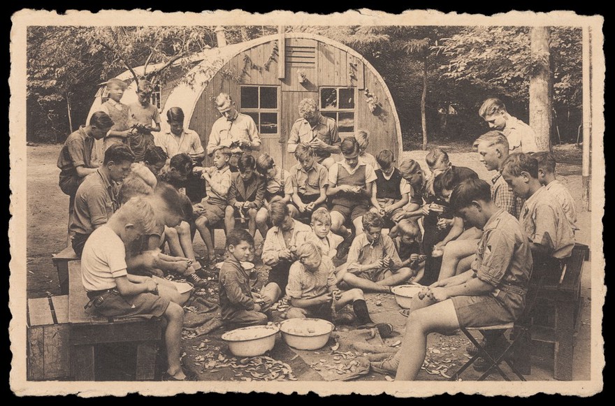 Scouts in a summer camp at Kapellen near Antwerp, peeling potatoes. Photographic postcard, ca. 1951.