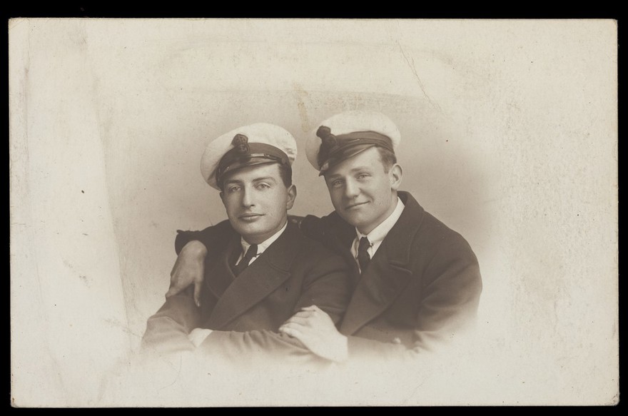 Two British naval officers in an intimate pose, one with his arms round the other. Photographic postcard, 192-.