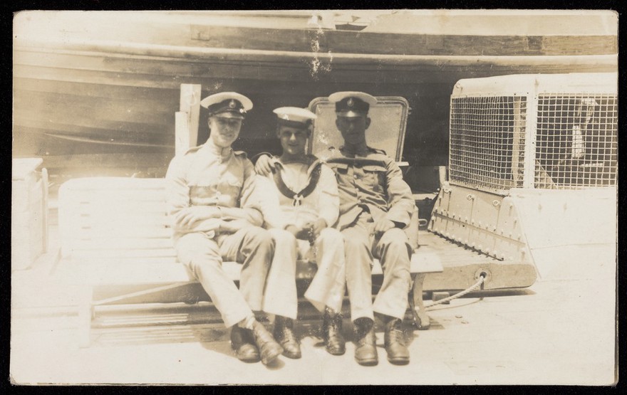 Two Marines and a young sailor sitting together on board ship. Photographic postcard, 192-.