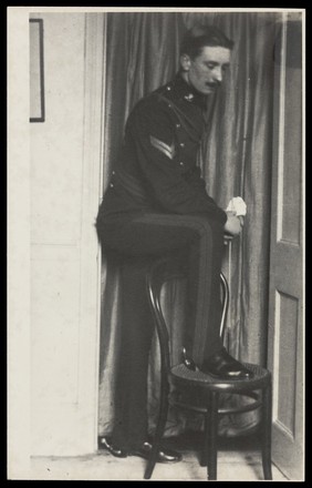 A Royal Fusilier places one foot on a chair to display his boots, ca. 192-. Photograph, 195-.