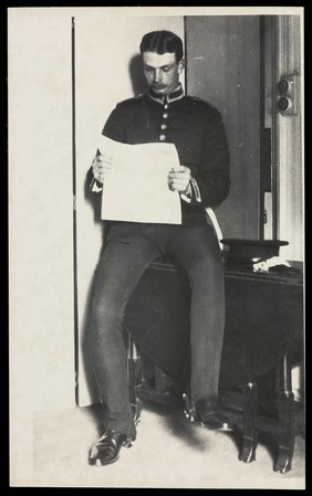 A Royal Fusilier seated reading a newspaper in a domestic setting, ca. 192-. Photograph, 195-.