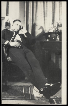 A Royal Fusilier leaning back in a chair in a domestic setting, ca. 192-. Photograph, 195-.